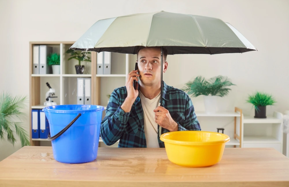 Man with umbrella under leaking roof