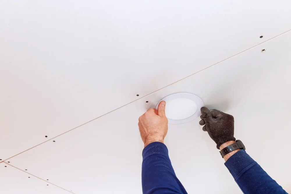 Skilled electrician is installing circular ceiling light at home