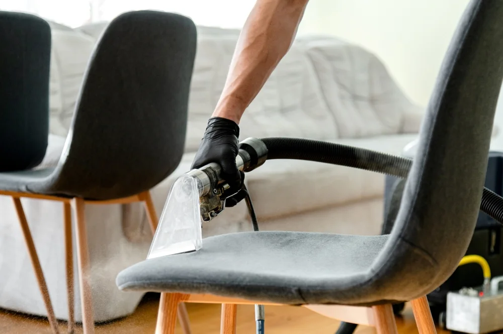 person is cleaning a gray chair  with vacume cleaner